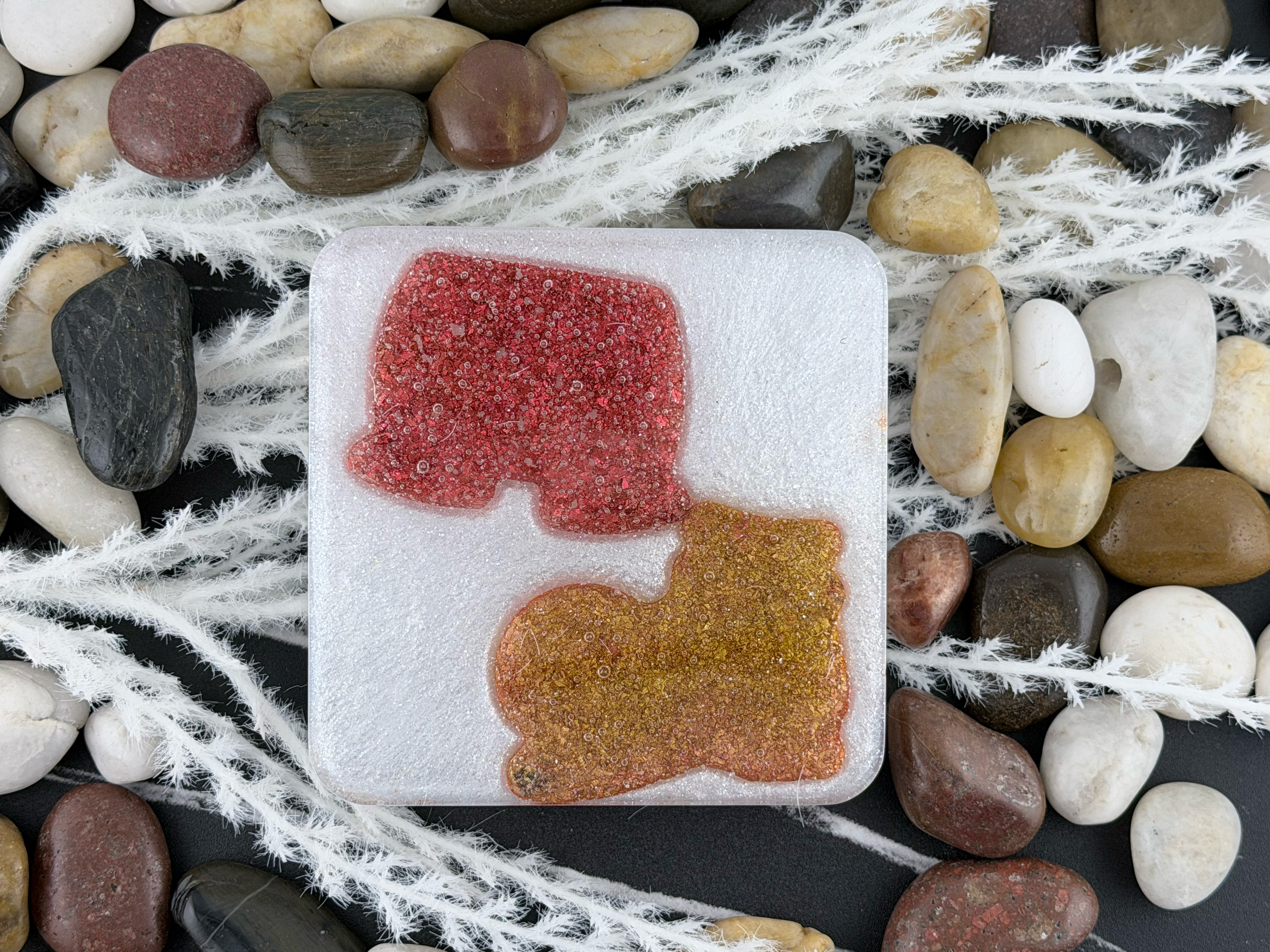 A square white resin coaster featuring Mickey Mouse's shorts and one of his shoes displayed on a bed of smooth river stones and white decorative grass.